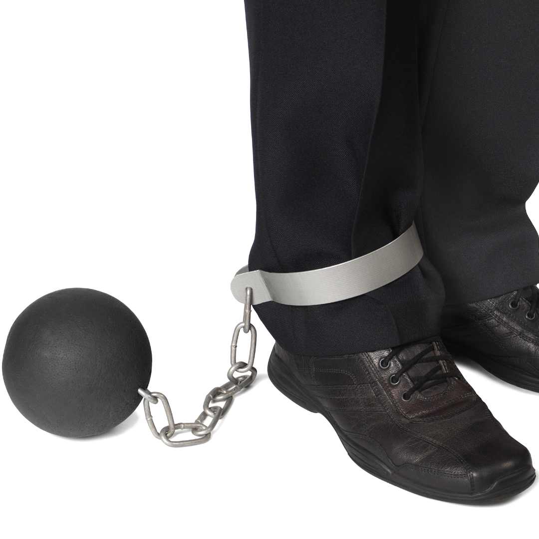 A man with a prison ball on his foot tight in. Just feets in business black shoes and black pants 
