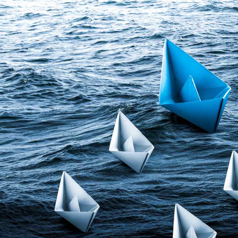 Leadership in a true meaning, one paper ship in front of others smaller ones 